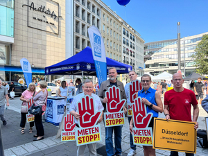 Die Fotos zeigen Personen, die sich an dem Aktionstag der Mietenstoppkampagne beteiligt haben. Die Menschen halten Transparente und Schilder hoch, auf denen z.B. „Düsseldorf braucht bezahlbarem Wohnraum“ oder „Wohnen ist keine Ware“ steht. Außerdem ist vielfach die sogenannte „Mietenstopp-Hand“ zu sehen. Es handelt sich um das Logo der Mietenstoppkampagne. Es handelt sich um eine erhobene Hand, die Einhalt gebieten soll.