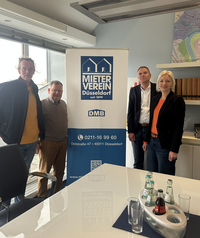 Auf dem Foto sieht man Harald Schwenk, Hans-Jochem Witzke, Claus Nesemann und Clara Gerlach im Sitzungssaal des Mietervereis. Die vier Personen stehen vor einem Banner mit der Aufschrift „Mieterverein Düsseldorf“.