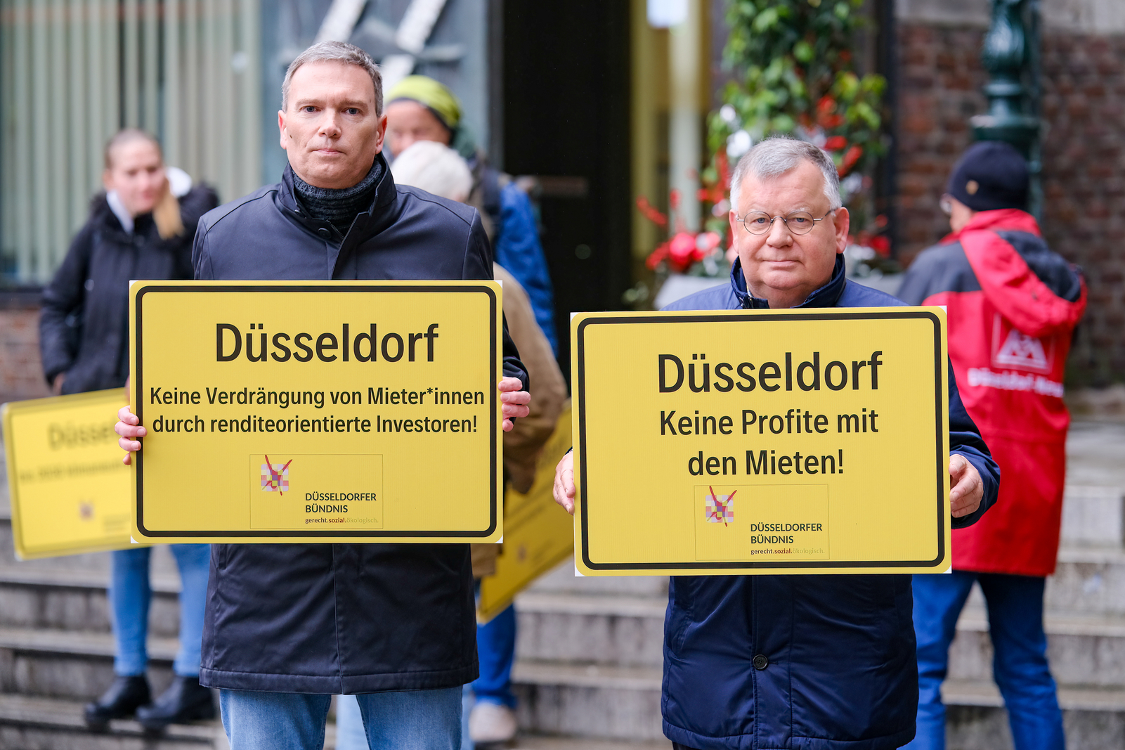 Foto: Michael Gstettenbauer Auf den beiden Fotos sieht man Hans-Jochem Witzke (1.Vorsitzender) und Claus Nesemann (Geschäftsführer) wie sie vor dem Düsseldorfer Rathaus Schilder mit den Aufschriften „Düsseldorf Keine Profite mit den Mieten!“ und „Düsseldorf Keine Verdrängung von Mieter*innen durch renditeorientierte Investoren“ hochhalten. Außerdem werden Bündnismitglieder gezeigt, wie sie ein Transparent mit dem Logo und dem Namen des Bündnisses hochhalten.
