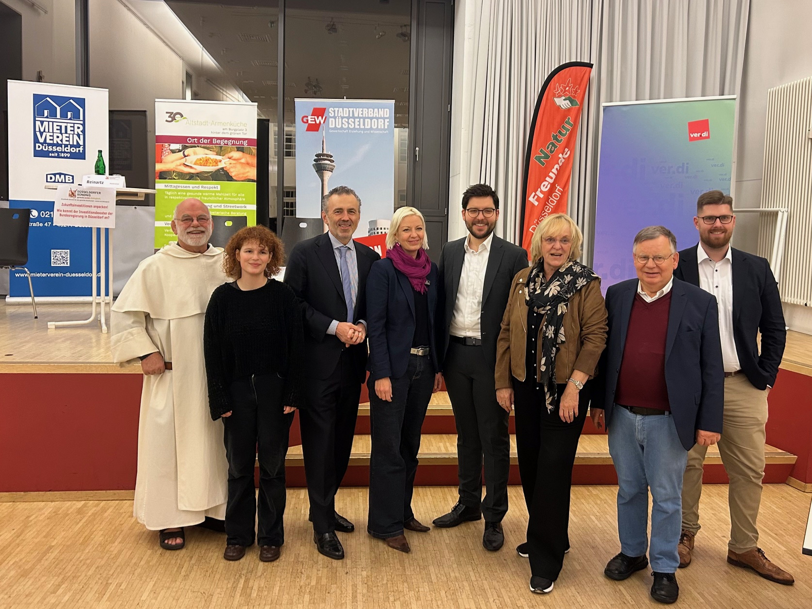 Auf dem Foto sieht man die o.g. Personen. Außerdem erkennt man im Hintergrund auf einer Bühne die Banner einiger Bündnismitglieder (Mieterverein Düsseldorf, Altstadt Armenküche, GEW,  Naturfreunde und Düsseldorf und ver.di).